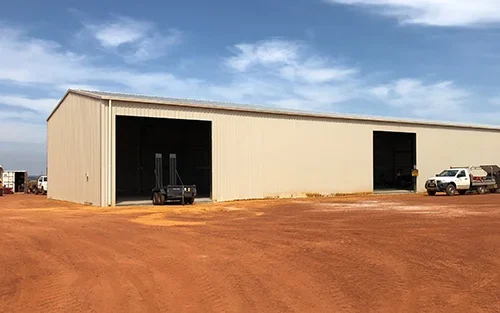 Photo of a large commercial shed clad in Colorbond Paperbark. The shed is surrounded by Utes.