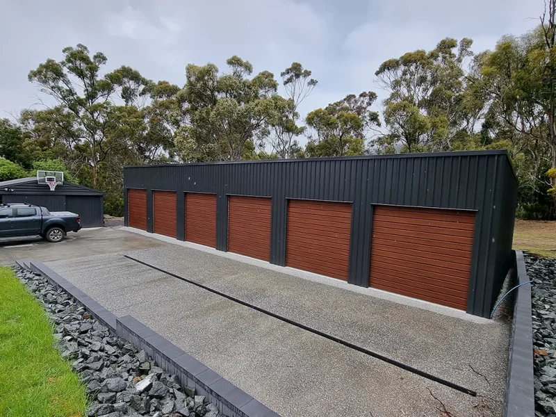 Australian-made garage with six bay woodgrain roller doors featuring Monument® roof and Monument® walls with landscaped surrounds