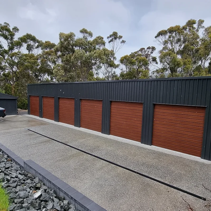 Australian-made garage with six bay woodgrain roller doors featuring Monument® roof and Monument® walls with landscaped surrounds